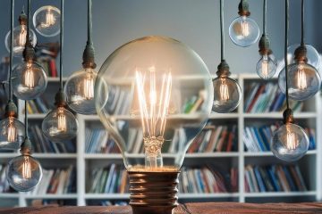 Lightbulbs hanging over a desk with a big lightbulb in the desk, bookshelf in background